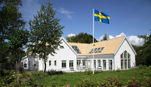 Svensk flagga och flaggstång framför ett hus